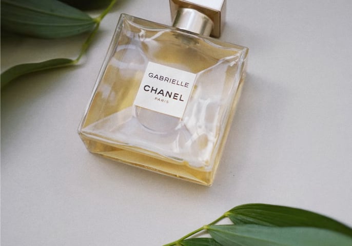 A Chanel perfume lying on the ground surrounded by some lush green leaves